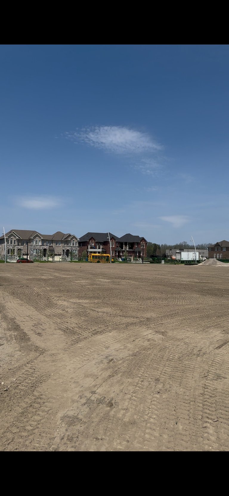 Row of new residential houses under construction on bare dirt land with blue sky and scattered clouds