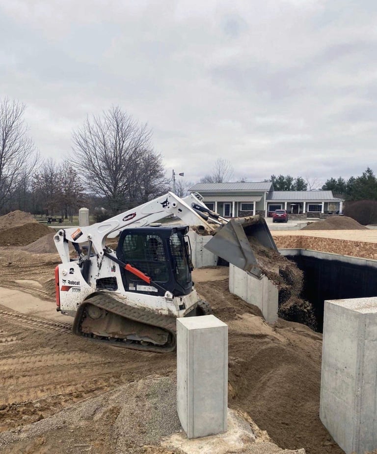 White compact track loader with raised bucket on a construction site surrounded by concrete foundation blocks.